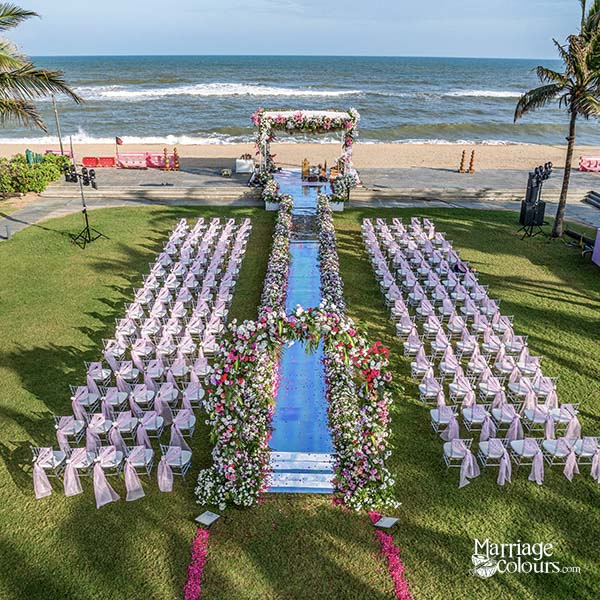 An aerial view of a beach wedding setup with a floral aisle, rows of chairs, and an ocean backdrop.