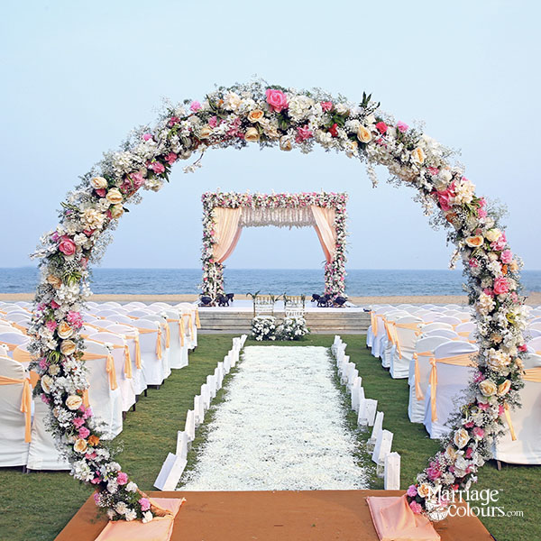 Beach wedding setup with a circular floral arch aisle and elegant mandap facing the ocean