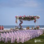 Beach wedding setup with floral mandap and pink decorated seating facing the ocean