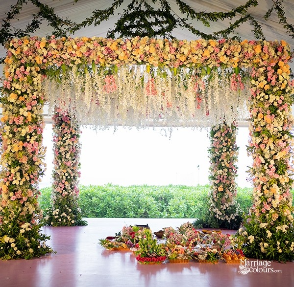 A grand floral archway decorated with a mix of pink, yellow, and white flowers, creating a vibrant and romantic backdrop.