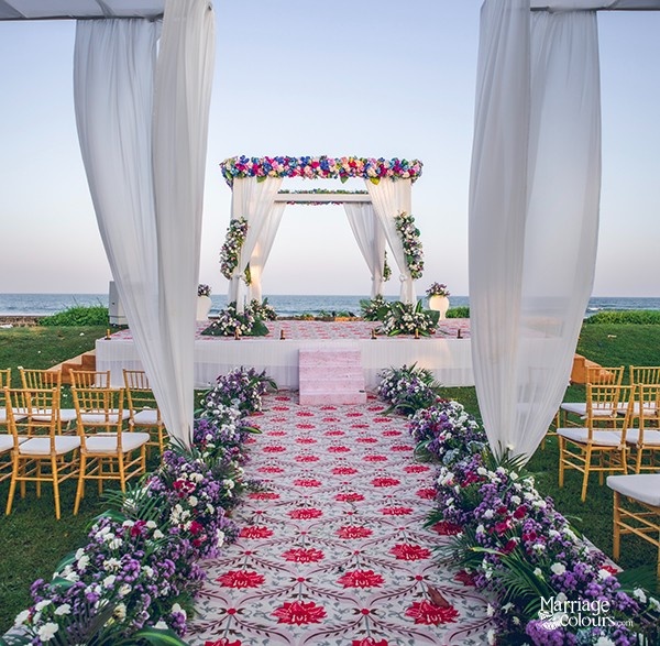 A traditional wedding mandap with golden chairs, colorful drapes, and floral decorations, set against a clear sky.