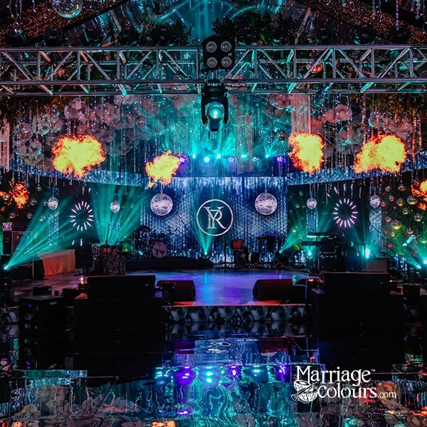 A vibrant stage setup with a large screen, colorful lighting, and a decorative backdrop featuring a monogram.
